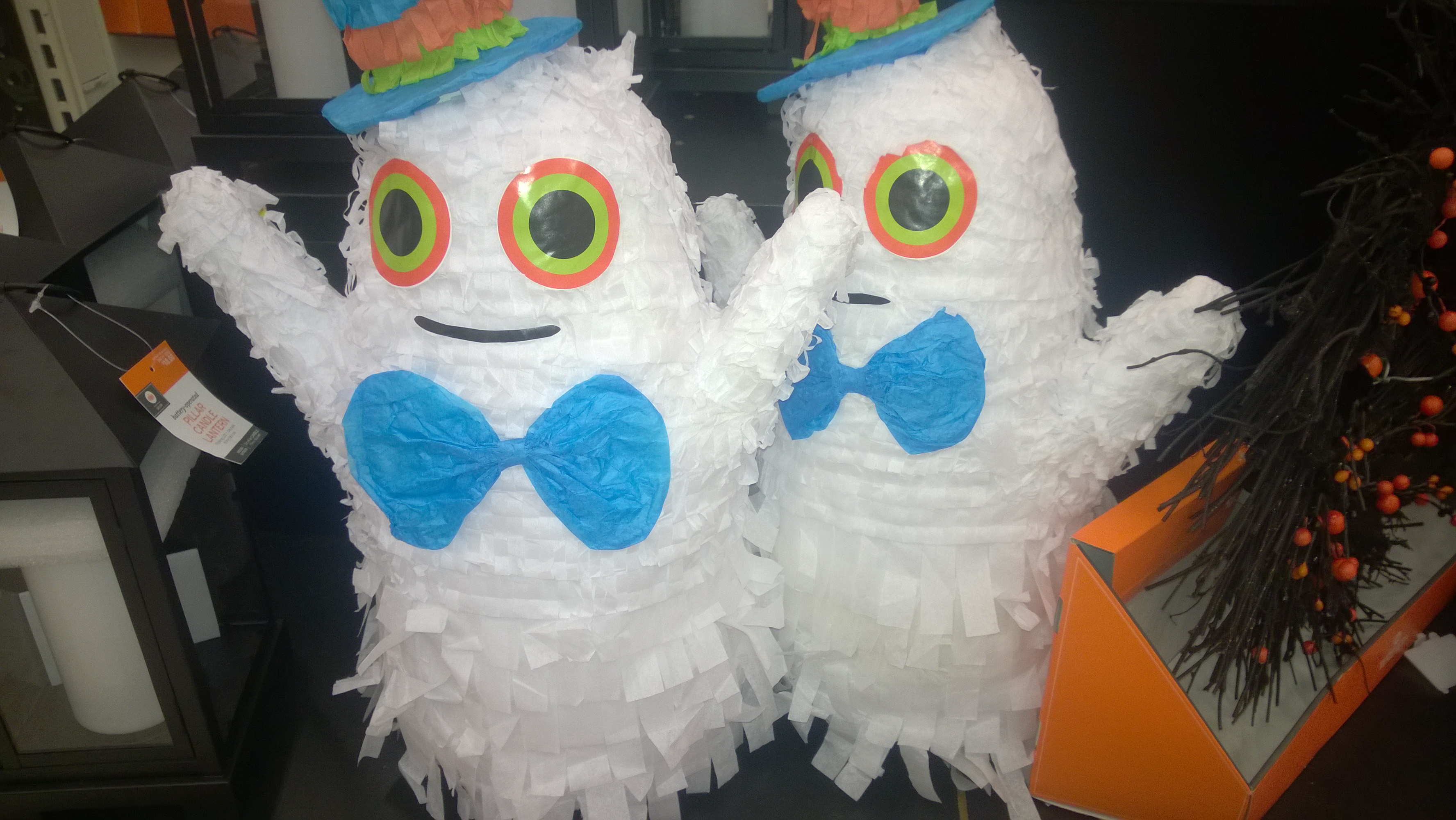 Two white ghost decorations with colorful hats and blue bow ties on a shop display.