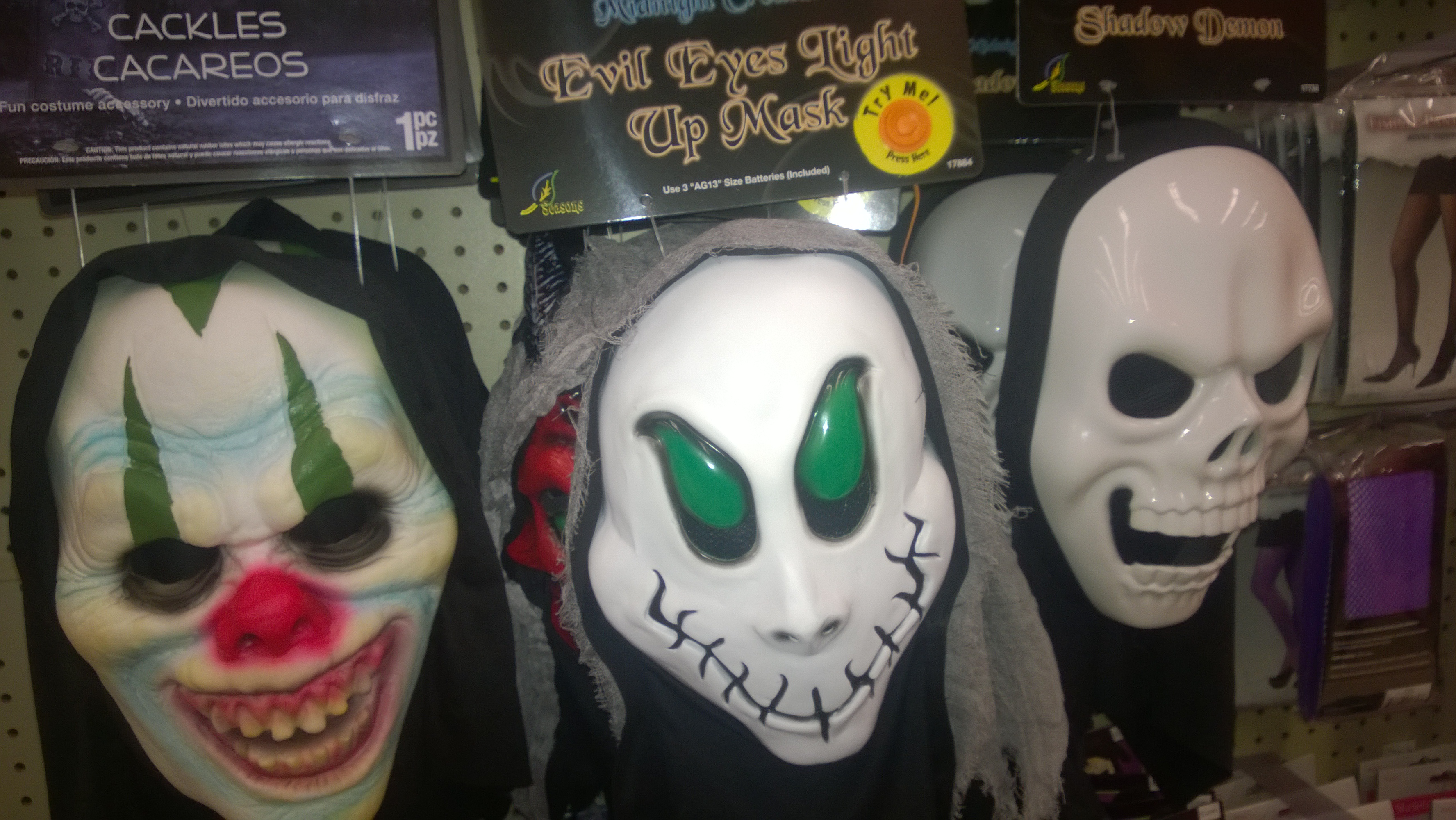A clown mask, a green-eyed white mask and a skull mask hanging on a retail display.